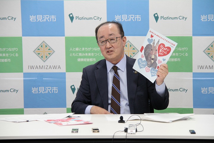 マヤマックスさんのデザインした出生届を手に持って掲げ、説明する松野市長の写真