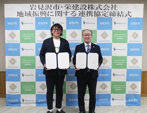 署名した連携協定書を開いて手に持ち、並んで立つ栄建設株式会社佛田社長と松野市長の写真