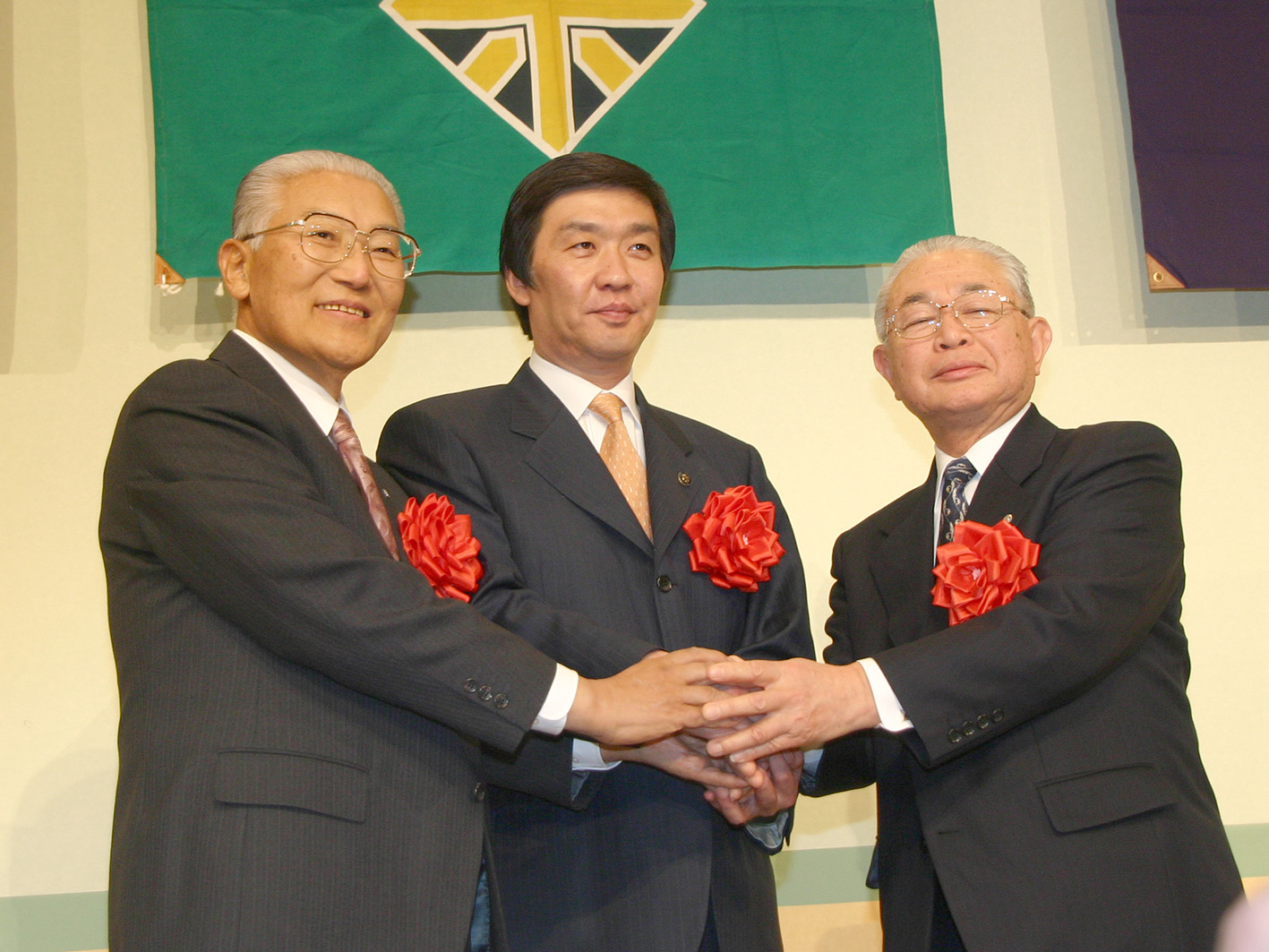 左胸に赤い花をつけた岩見沢市長、北村長、栗沢町長の3人が握手をしている合併協定調印式の写真