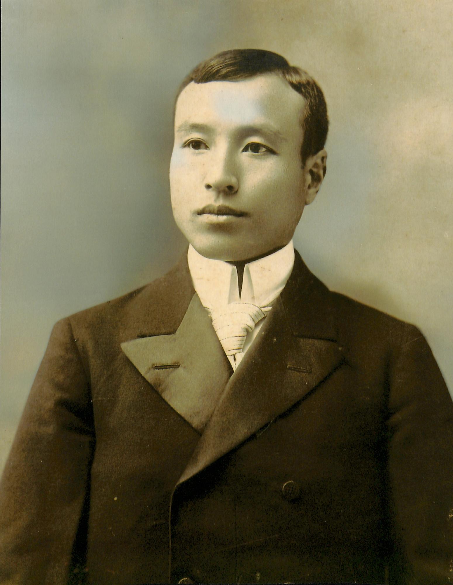 白いシャツとネクタイに黒のスーツ姿で少し左上を向いた、北村雄治のモノクロ写真