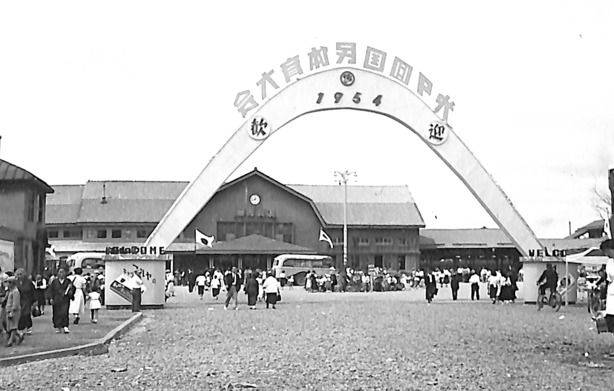 第9回国民体育大会の開催を関係する歓迎するゲートが設置され、多くの人が行き交う昭和29年の岩見沢駅前のモノクロ写真