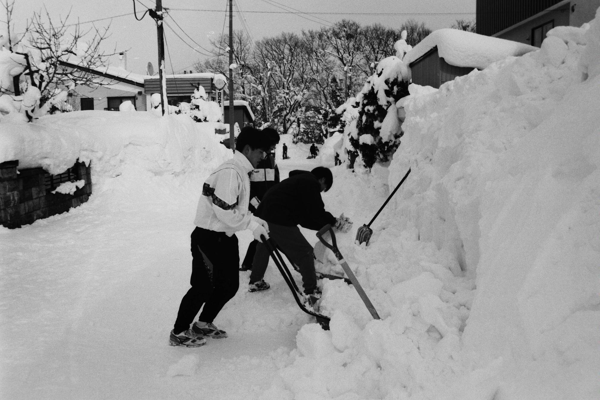 身長より高く積もった通路わきの雪の除雪をしている高校生のボランティア除雪の様子が写った写真