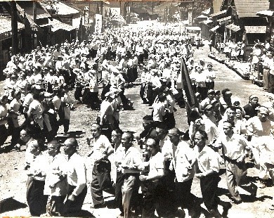 商店街の街道をデモ隊が行進し、たくさんの人が集まっている、三山分離撤回のデモ隊を迎える商店会の昭和35年の白黒写真
