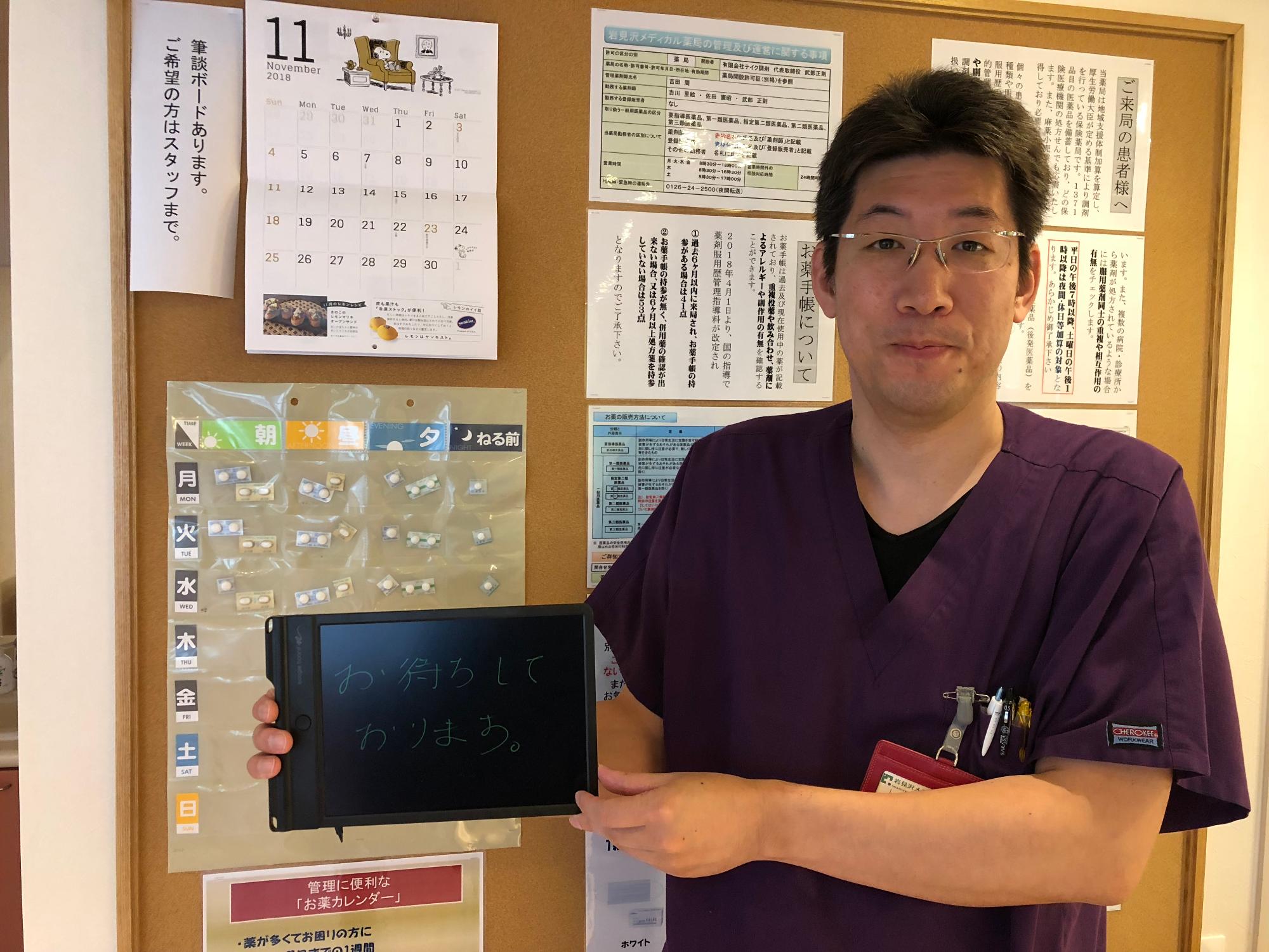 筆談ボードを横に掲げてはにかむ男性の写真