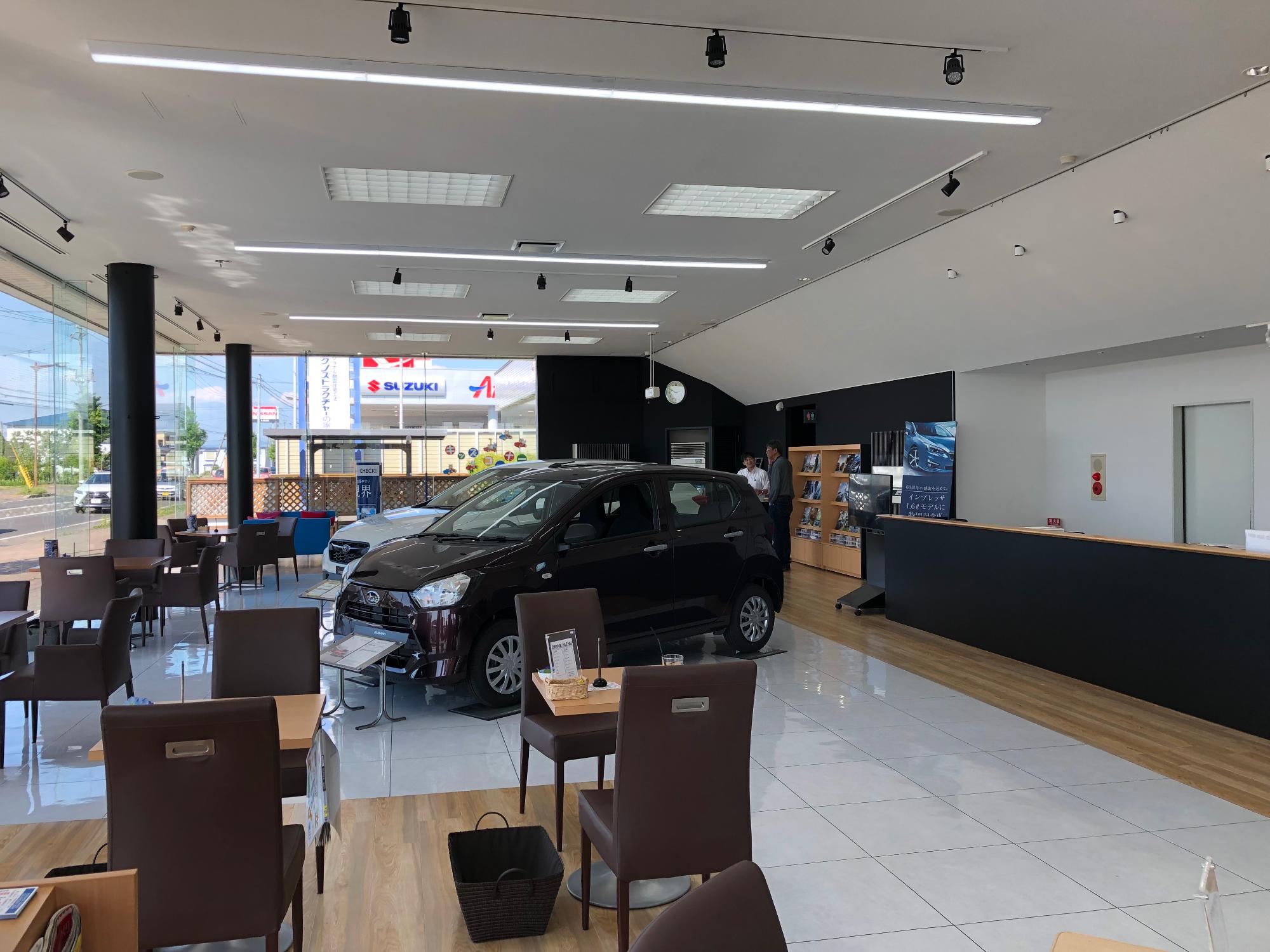 休憩・説明向けの机と椅子に囲まれるようにスバルの車が展示されている写真
