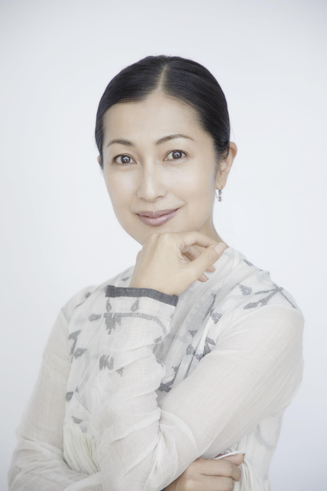 手の甲を顔に沿え、こちらに向かいほほ笑む鶴田真由(つるたまゆ)さんの写真