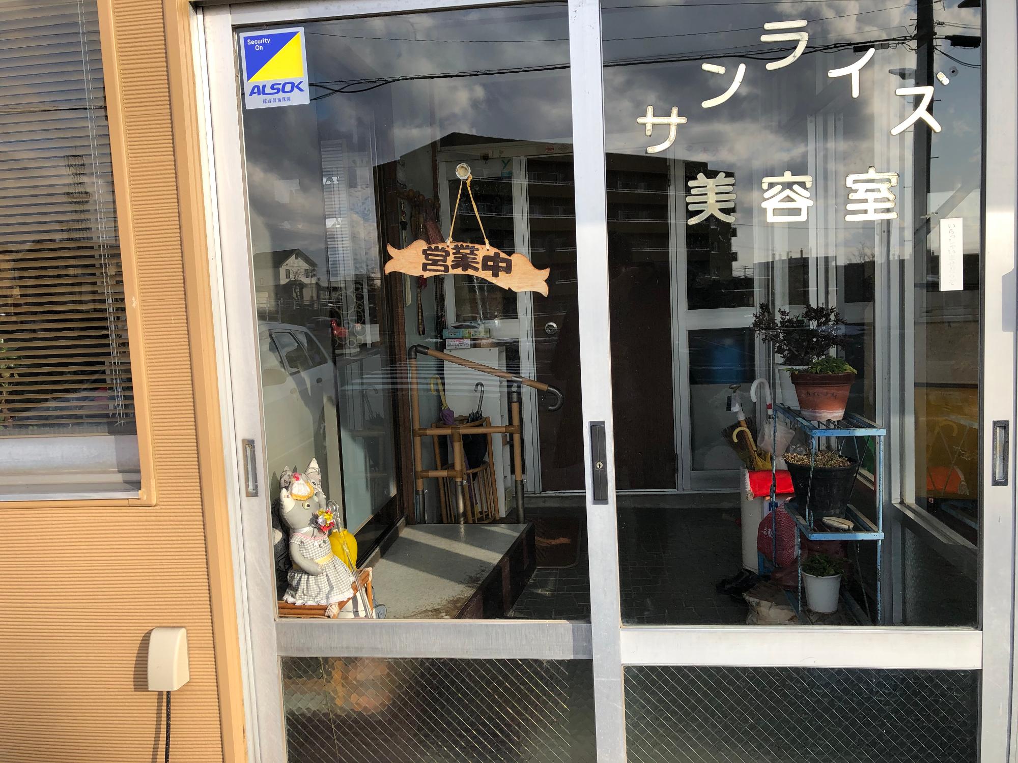 「営業中」と書かれた木製のかけ看板があるサンライズ美容室入り口の写真