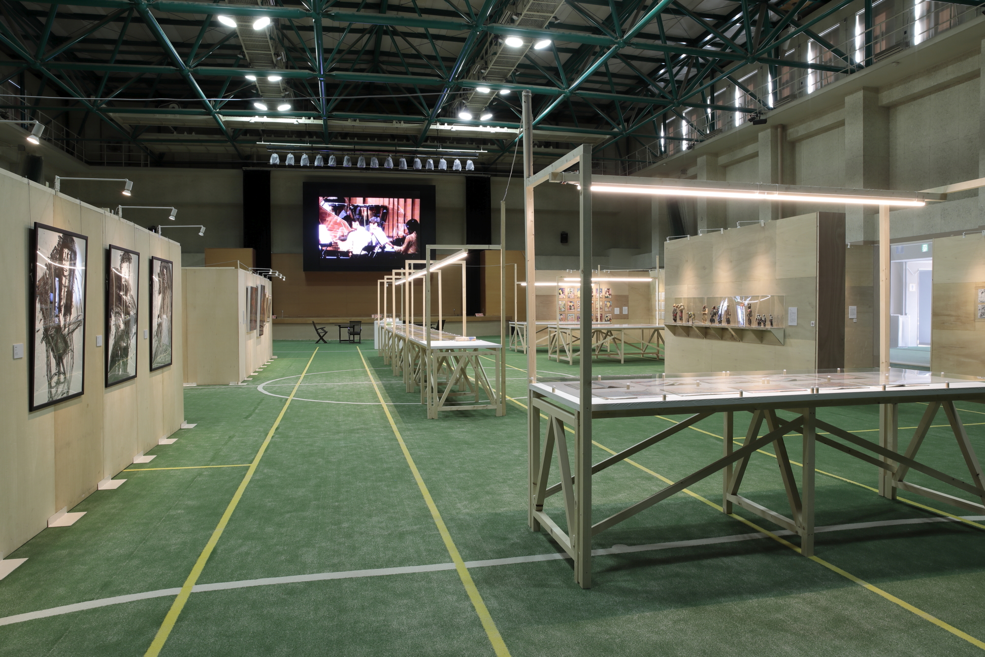 体育館に設置された映像が映し出されたモニターと、絵画や様々な作品が展示されている写真