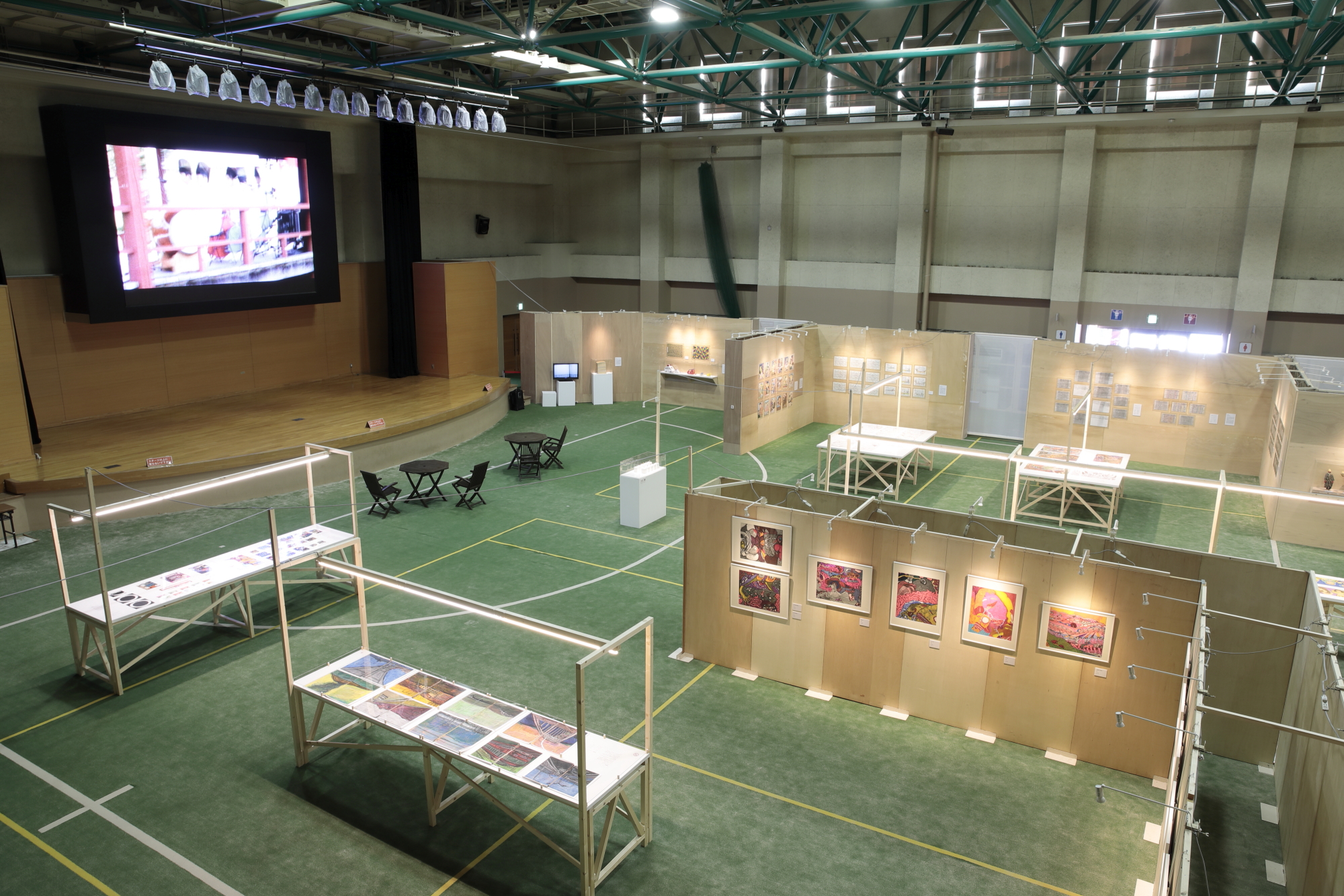 体育館に設置されたモニターと、展示会全体の様子がうかがえる全体写真