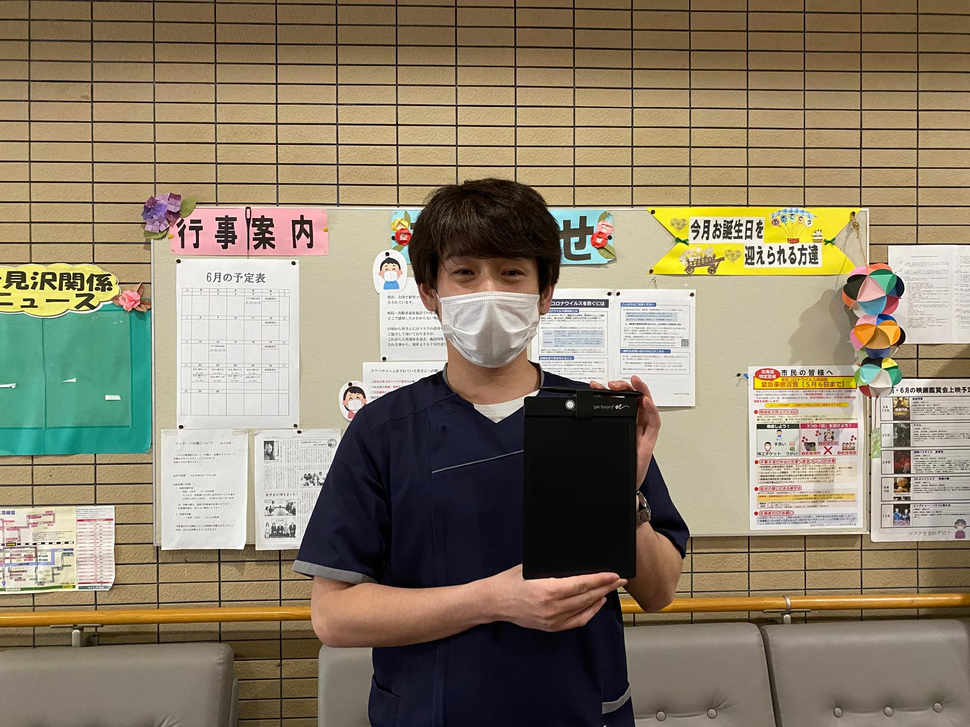 筆談ボードを掲げてほほ笑む男性の写真