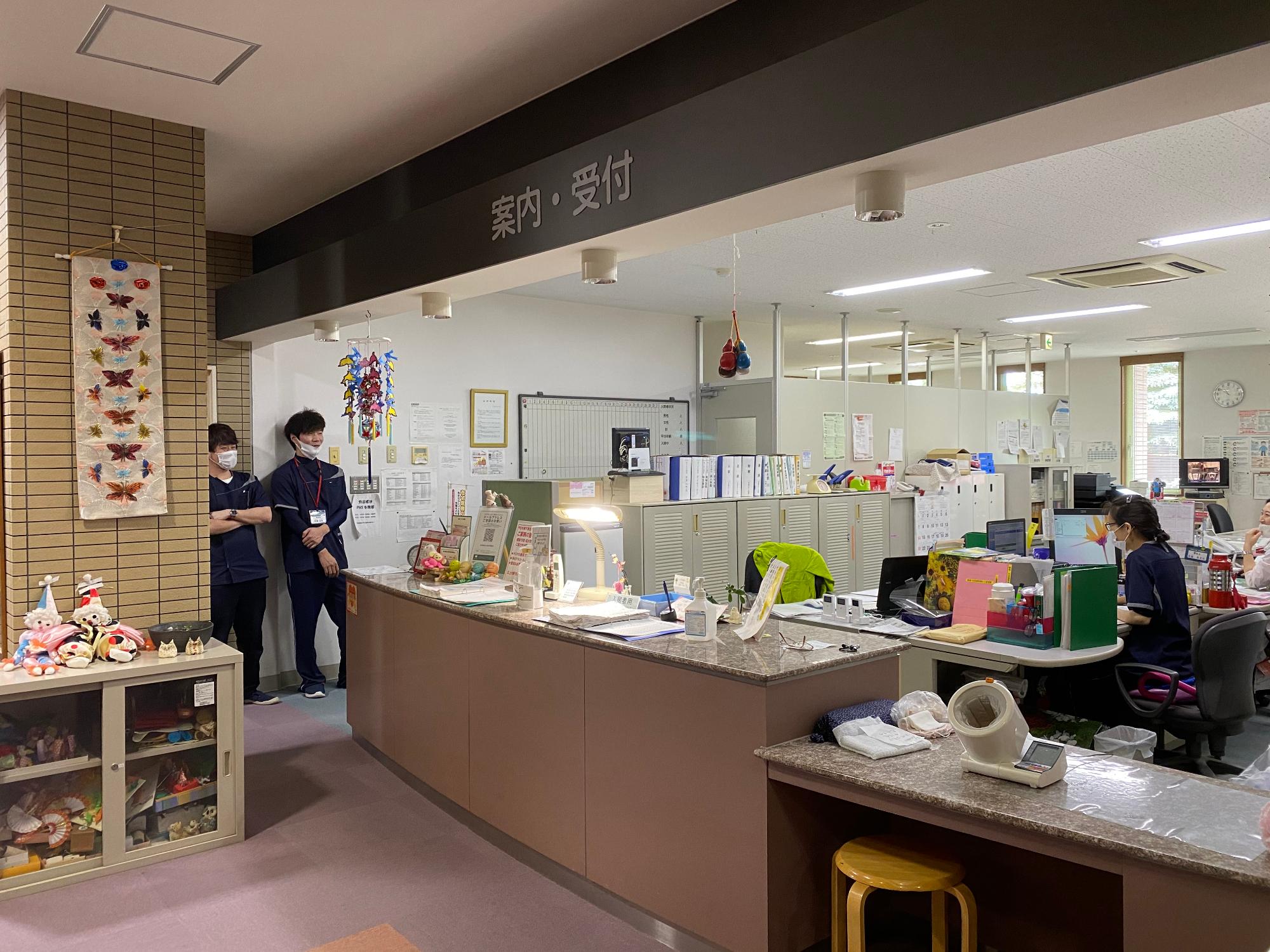 床やカウンターがあずき色でそろえられた温かみのある雰囲気の案内受付の写真