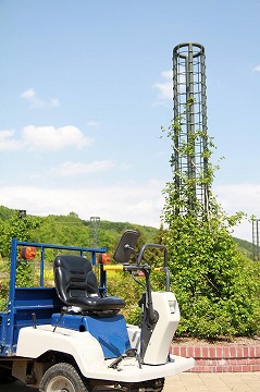 左手前に作業用のカート、背景に咲く前のバラや青空が写っている写真