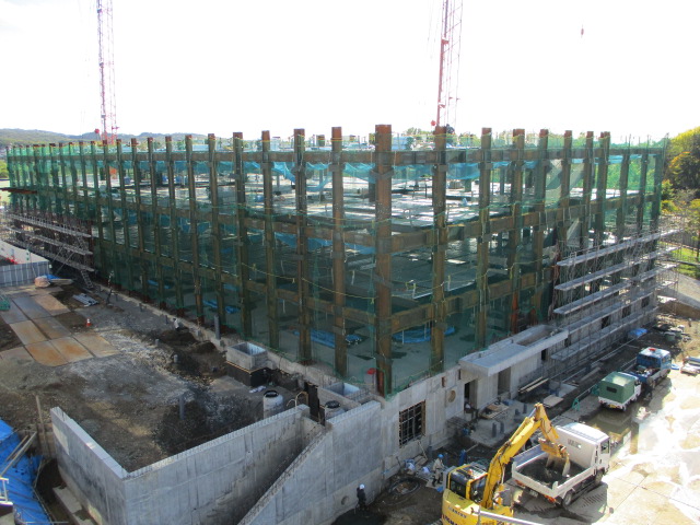 工事中の様子を外から撮影した写真。柱がむき出しとなっている3階建ての大きな建物が見える。