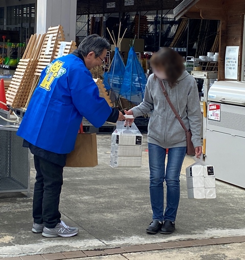 青いハッピを着た男性が選挙啓発物品のポケットティッシュを女性に渡している様子の写真