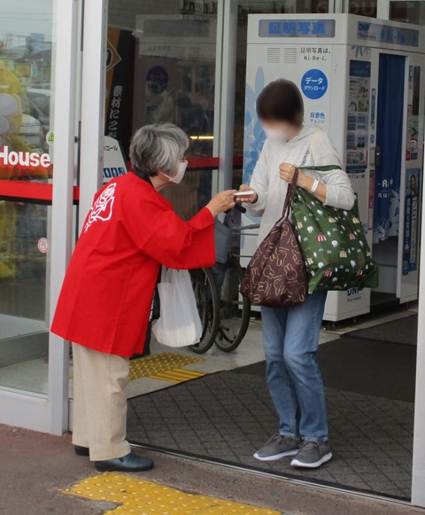 赤いハッピを着た女性が選挙啓発物品のポケットティッシュを女性に渡している様子の写真