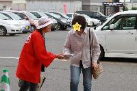 赤いハッピ姿の女性が選挙啓発物品を女性に渡している様子の写真