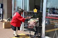赤いハッピを着た女性が選挙啓発物品を買い物帰りの女性に渡している様子の写真