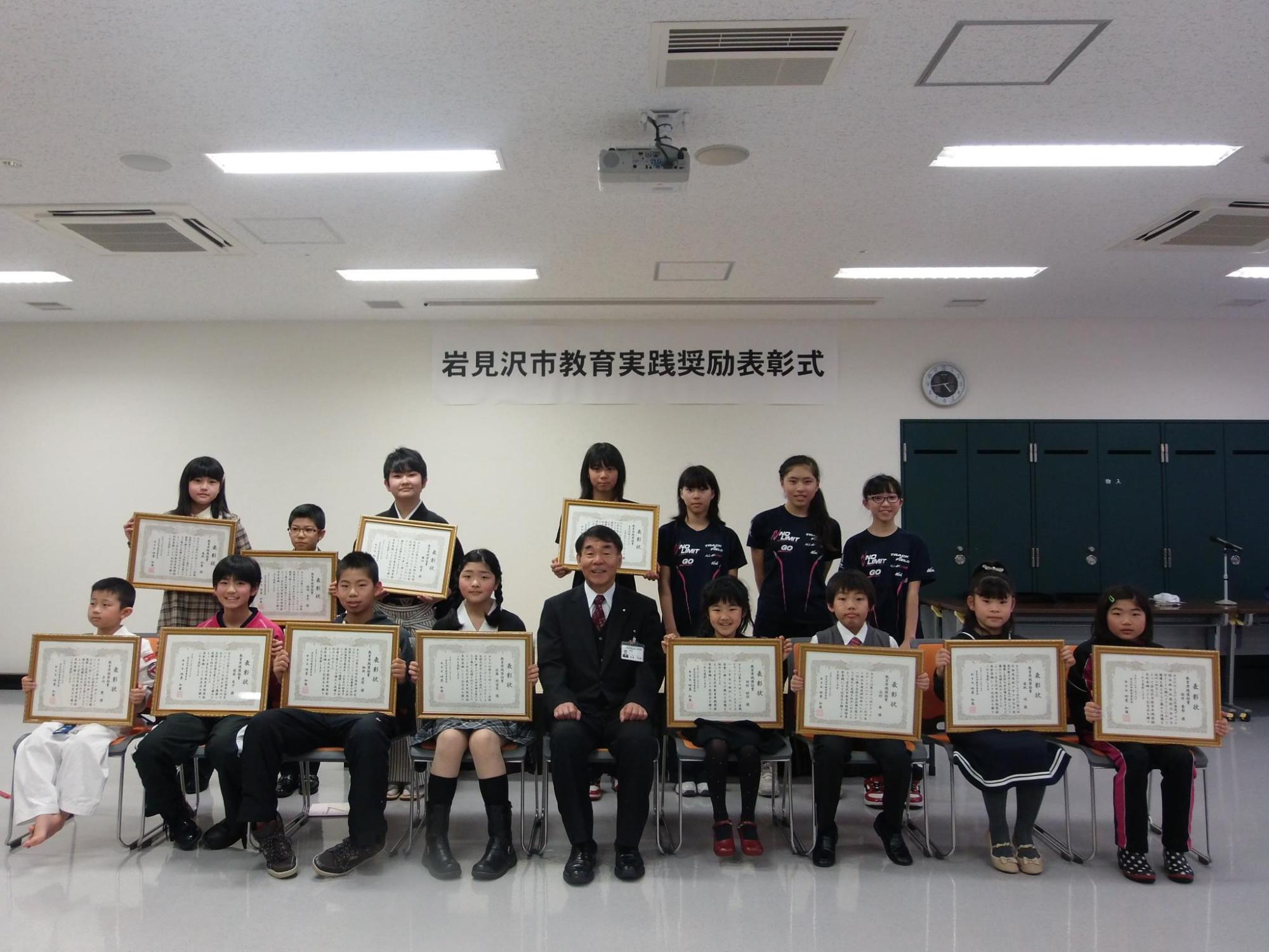 盾に入った賞状を手に持った受賞者の集合写真
