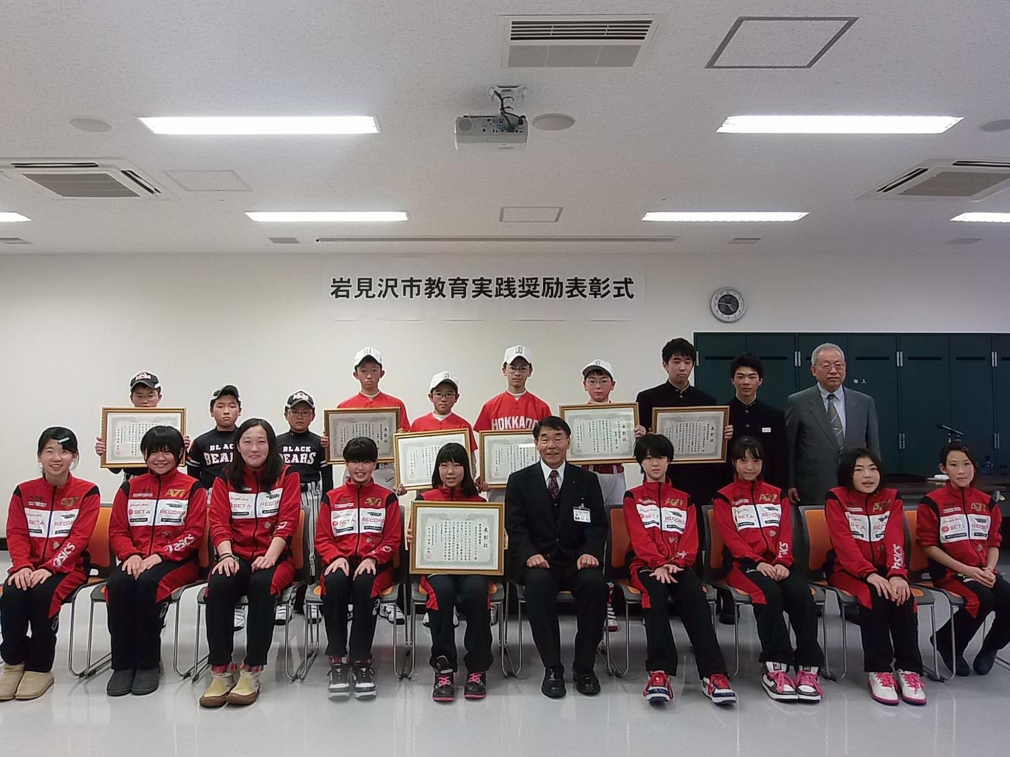 盾に入った賞状を手に持った受賞者の集合写真