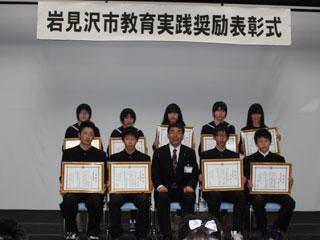 表彰式で座る光陵中学校の受賞者の男女と中央の男性の様子の写真