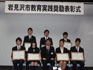 表彰式で座る高校の受賞者の男女と中央の男性の様子の写真