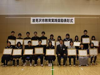 個人受賞者の小中学校の表彰式に立つ数人の男女と椅子に座る数人の男女の様子の写真