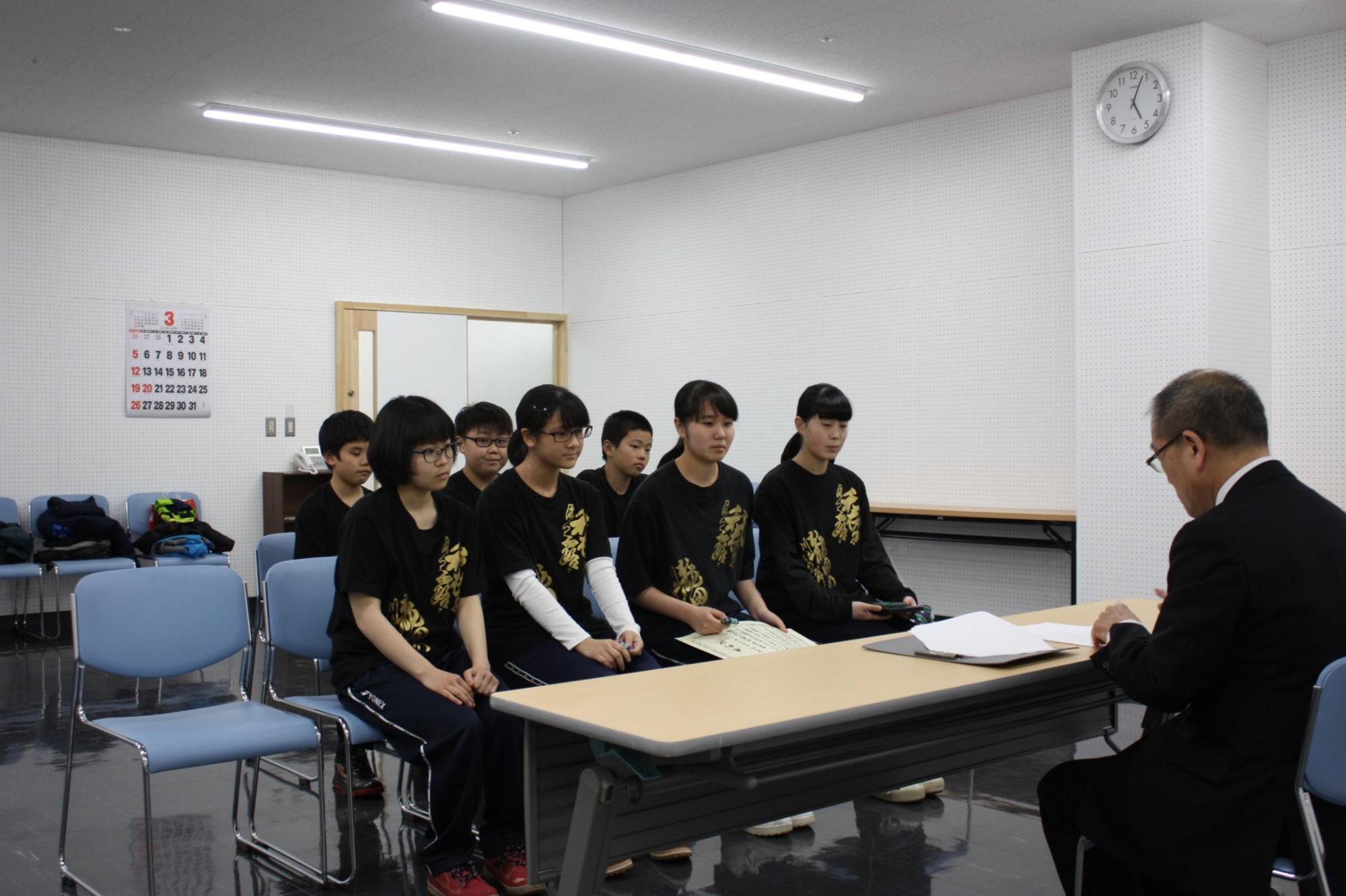 教育長と机を挟んで、7人の生徒が椅子に座っている様子