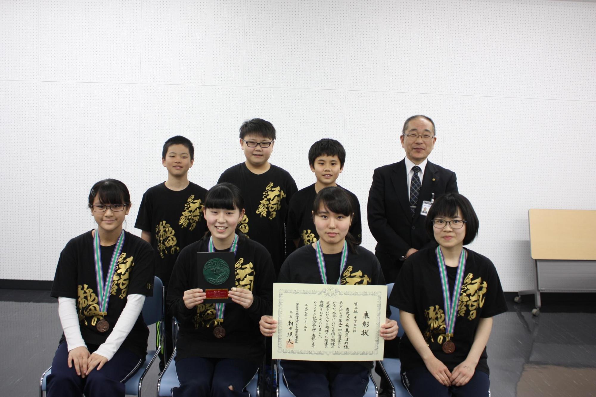 前列に4人、後列に3人のユニフォーム姿の生徒とその隣に並んだ教育長の笑顔の記念写真