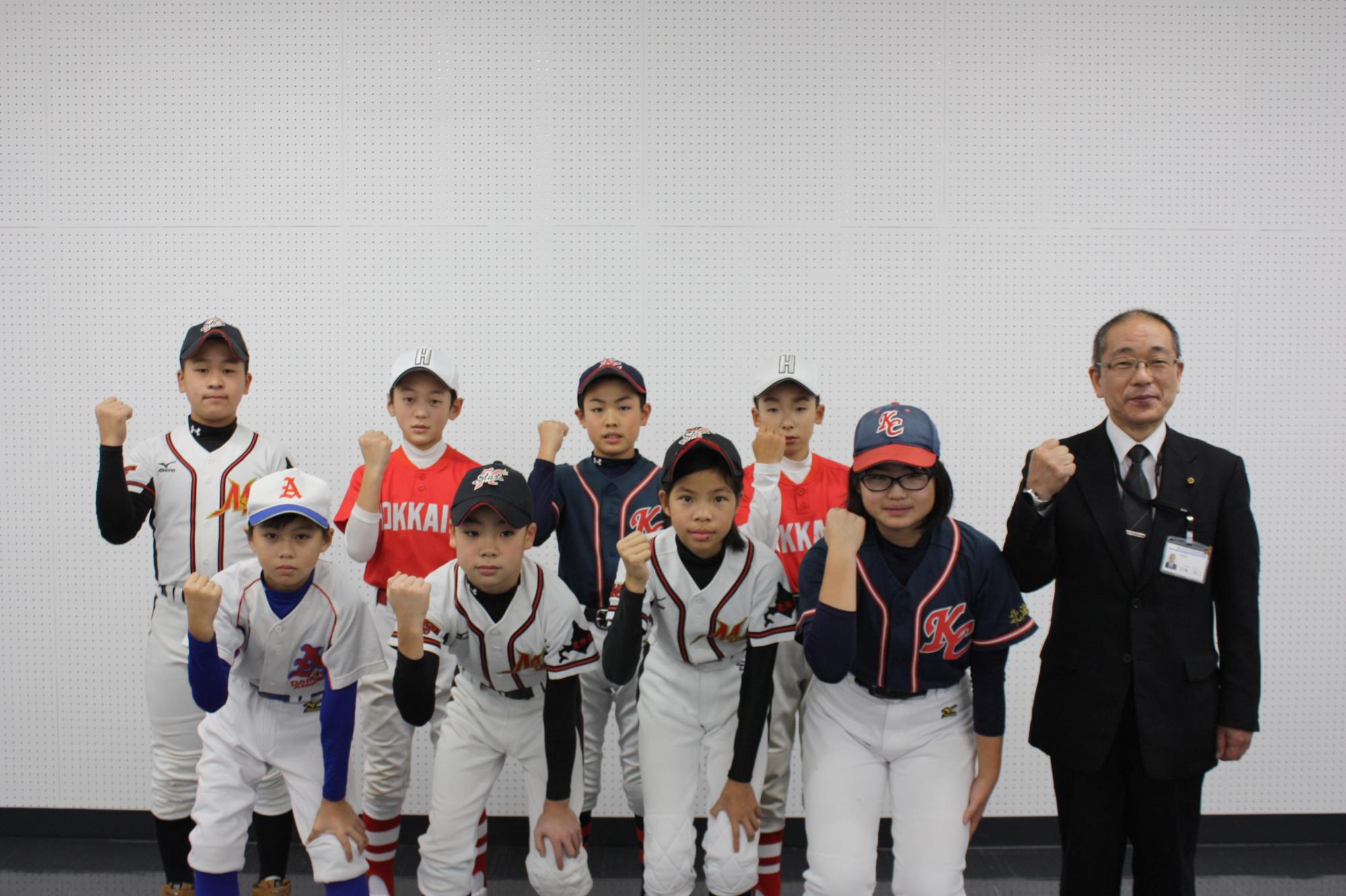 ユニフォーム姿の選手が前列に4人、後列に4人、その右横に教育長が立ち並び、右手をガッツポーズして撮った記念写真