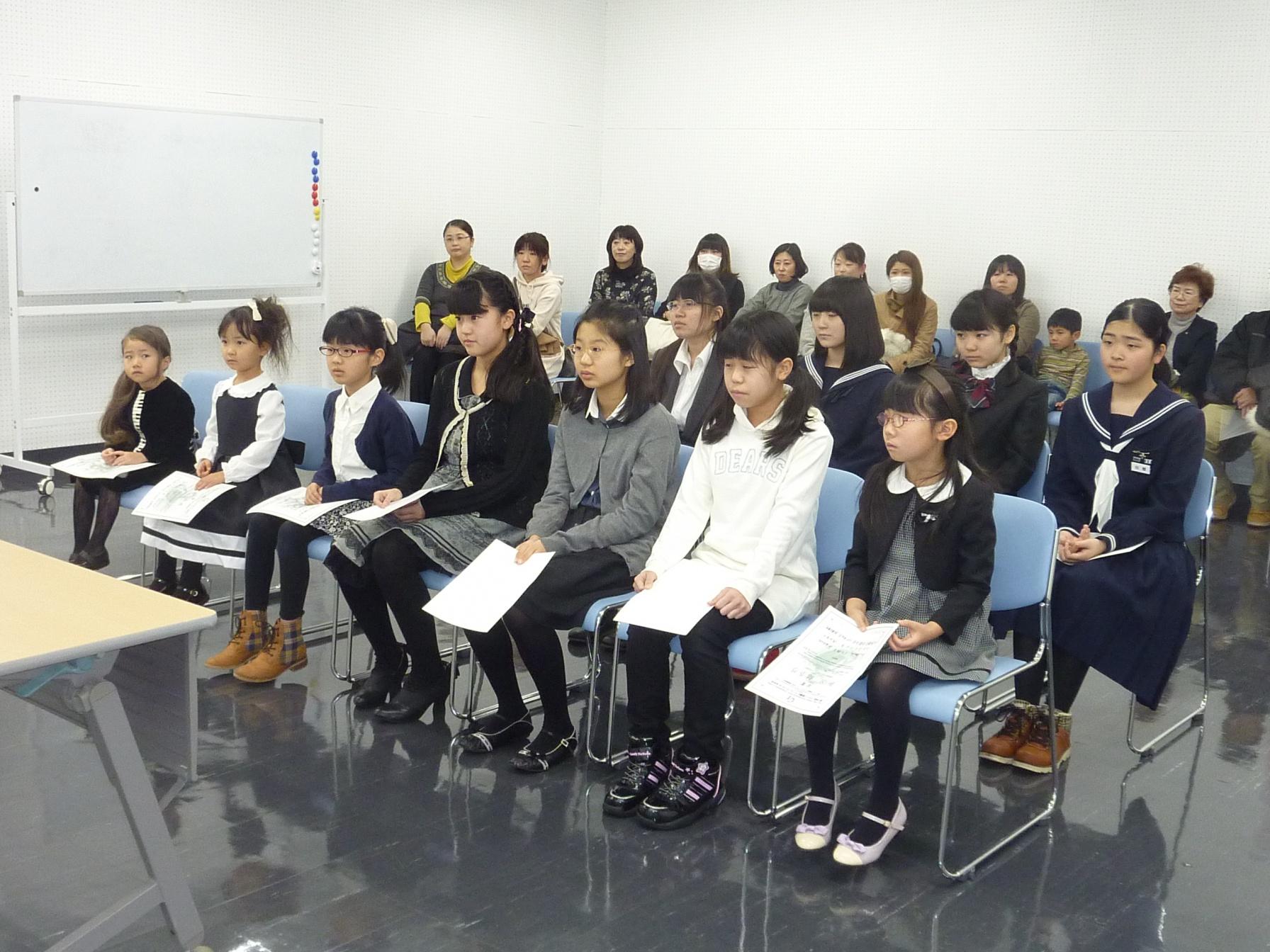 前列に7人、後列に4人、賞状を持った入賞者が椅子に座っている様子