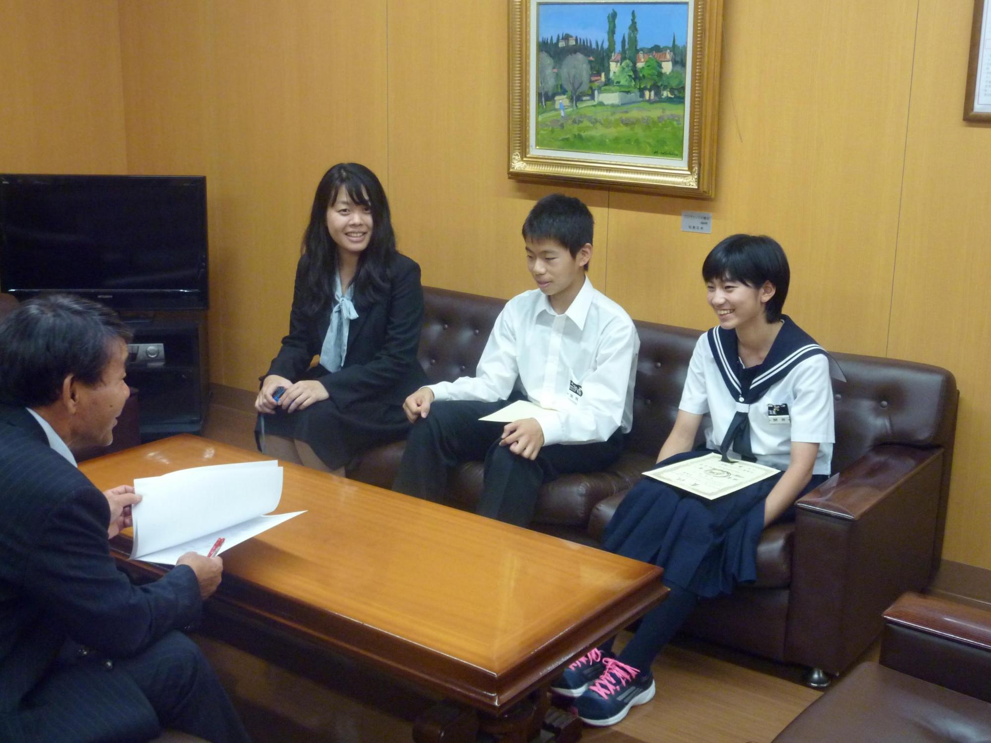 教育長と向かい合い笑顔で話す細岡さんと開発さんと女性の写真
