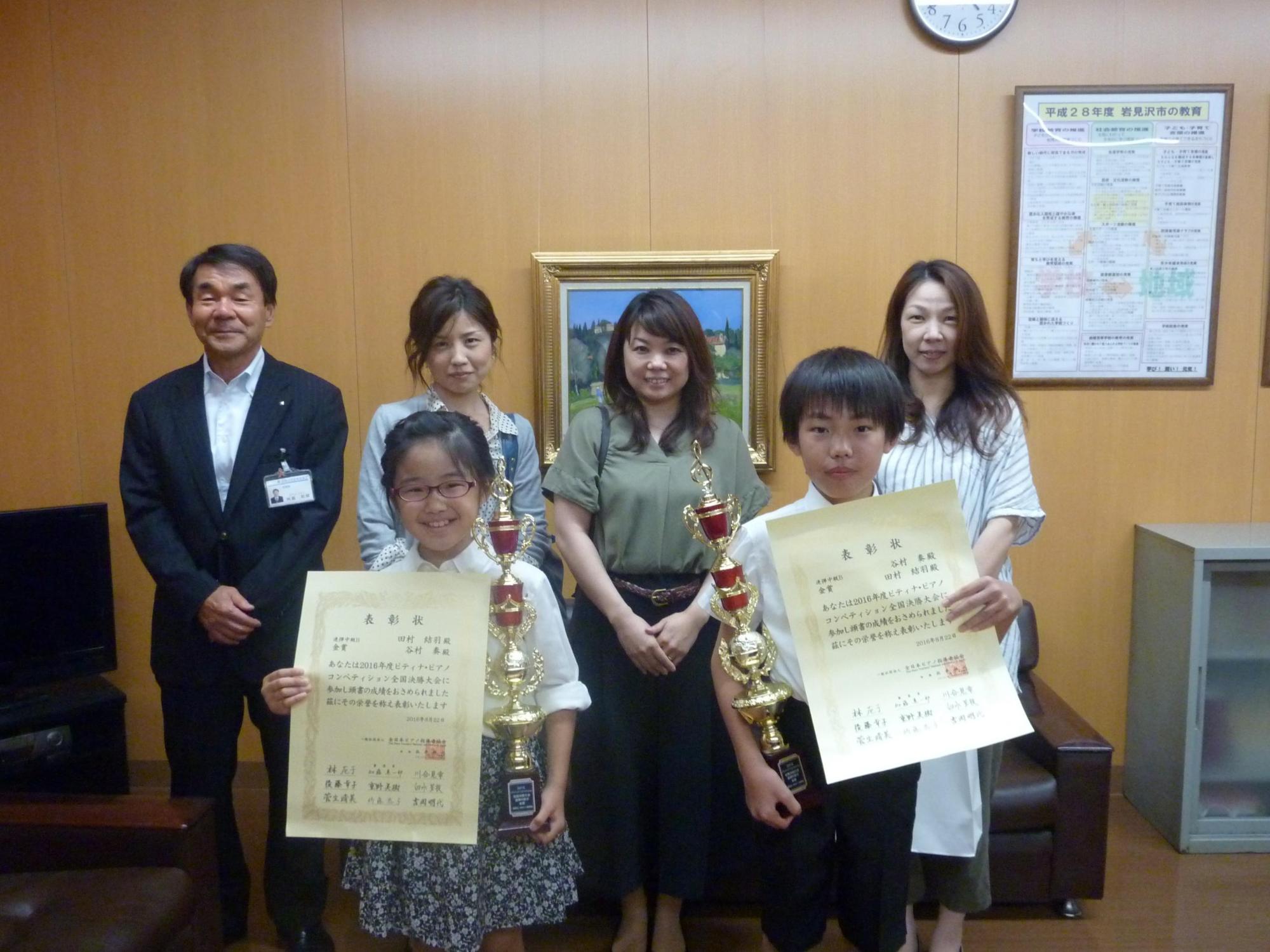 賞状とトロフィーを持つ谷村さんと田村さんの後ろに教育長と女性3人が立つ写真
