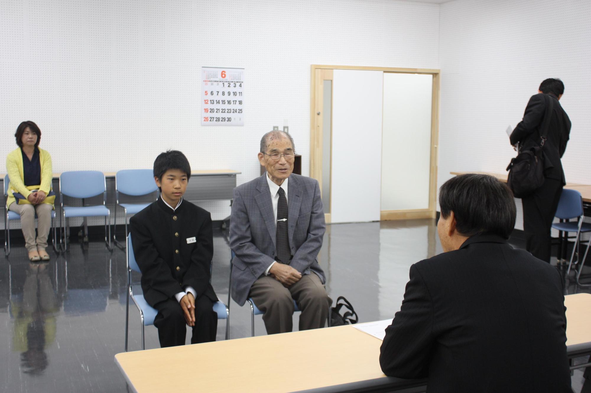 太田さんと男性が並んで座り、向かいの教育長の話を聞いている様子の写真