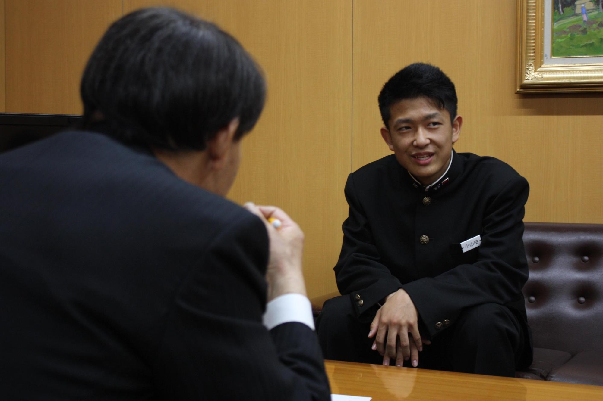 教育長と小山田凌さんと撮影した写真。二人ともソファに腰かけ、机を挟んで話をしている。