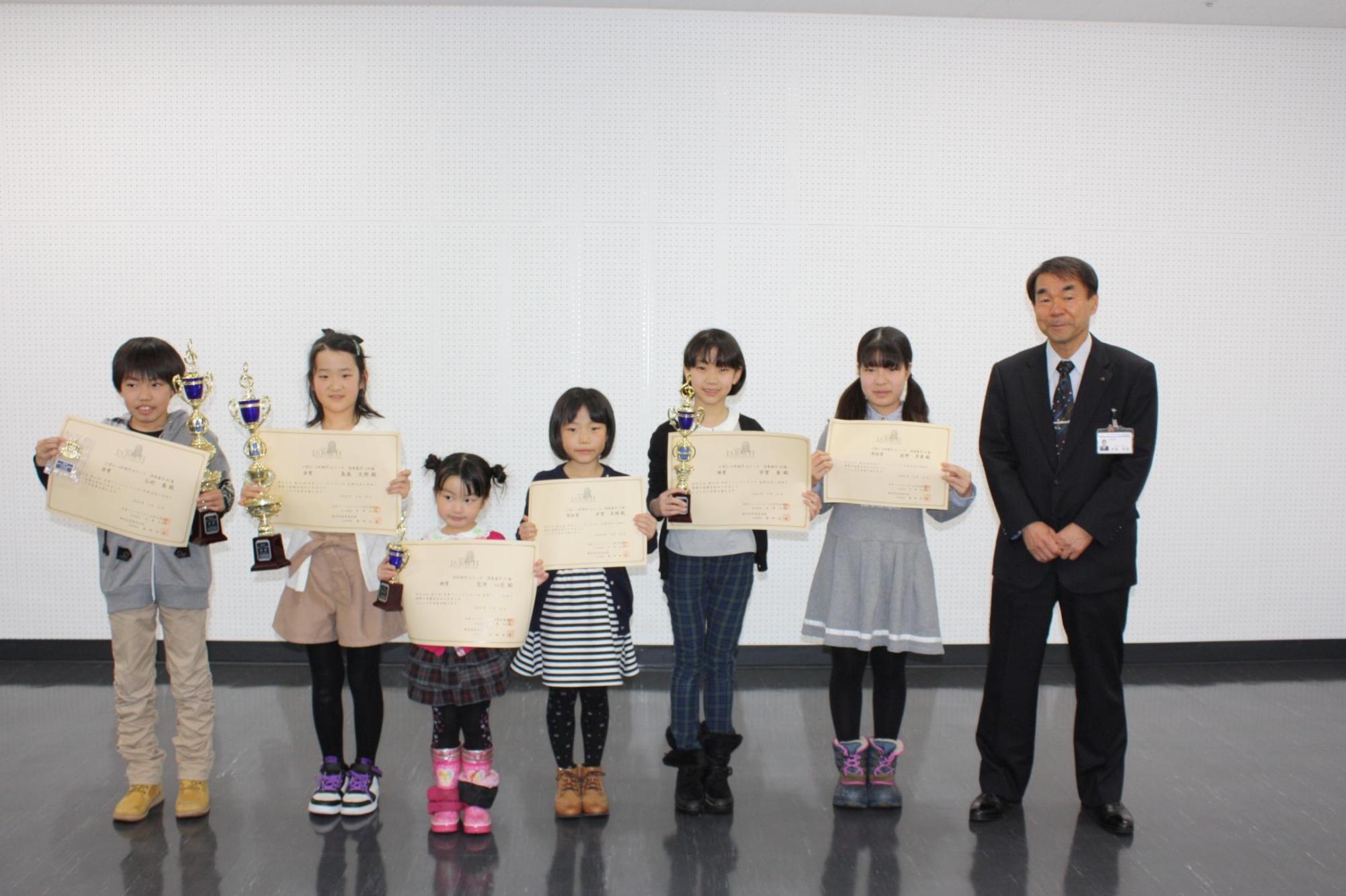 賞状を持った6人の男女の子供と教育長を撮影した写真。