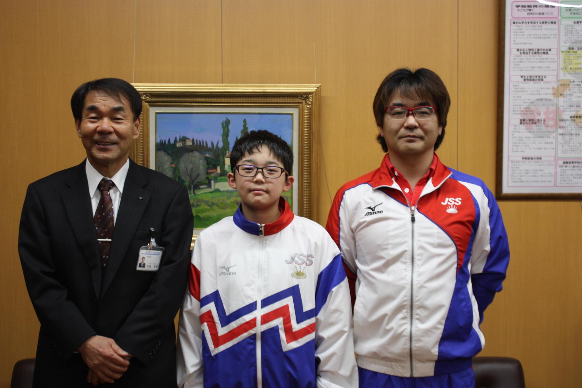 教育長と一人の子供ともう一人の大人が正面を向いて記念撮影をしている写真。
