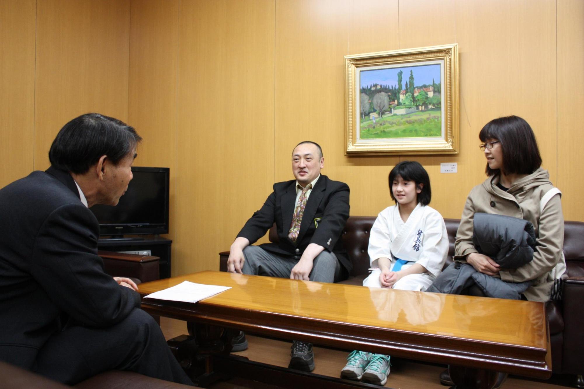 机を挟んで、教育長と空手道着を着た子供ともう二人の大人が話をしている写真。