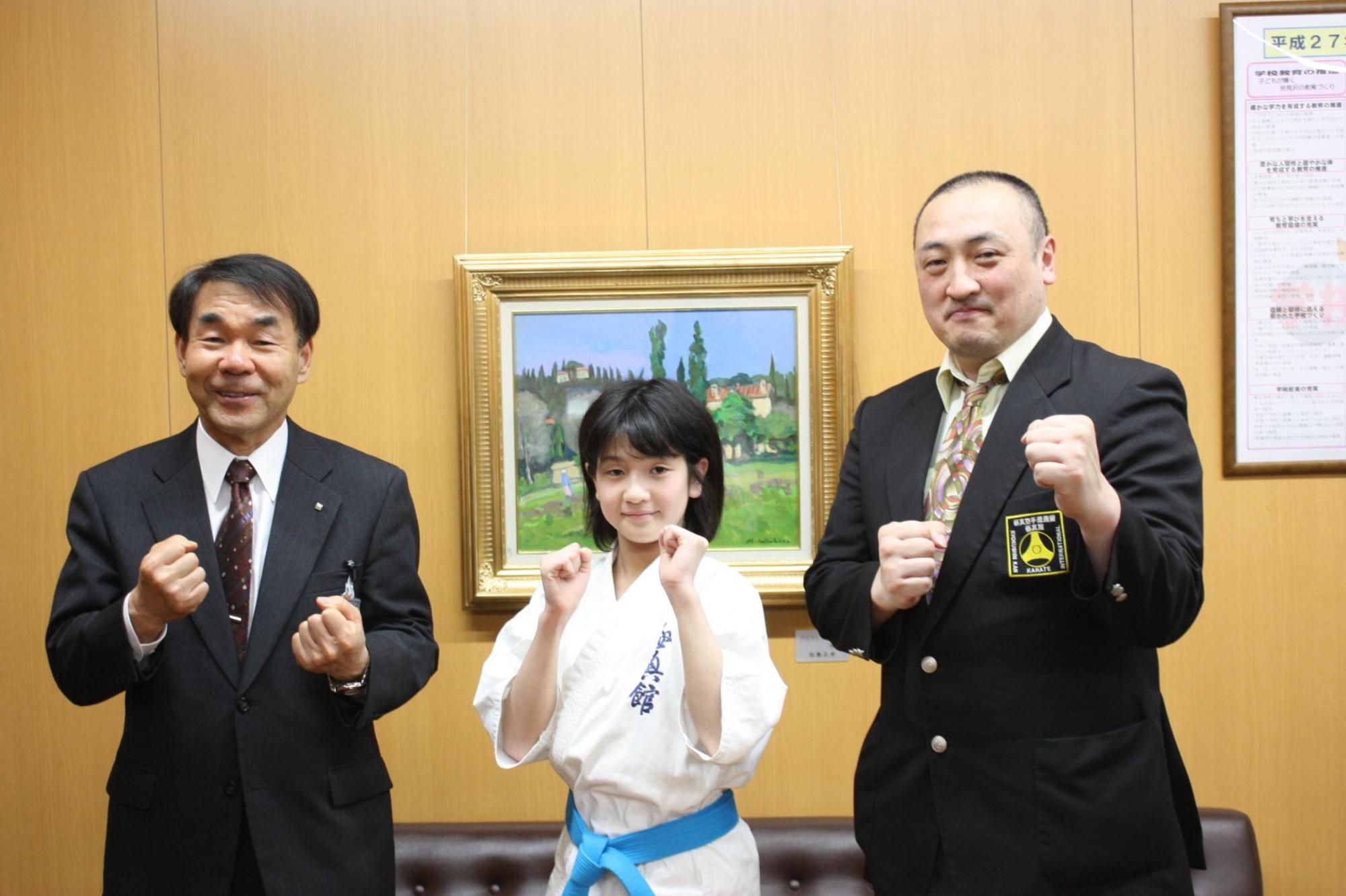 教育長と空手道着を着た子供と、もう一人の大人がガッツポーズをして記念撮影をした写真。