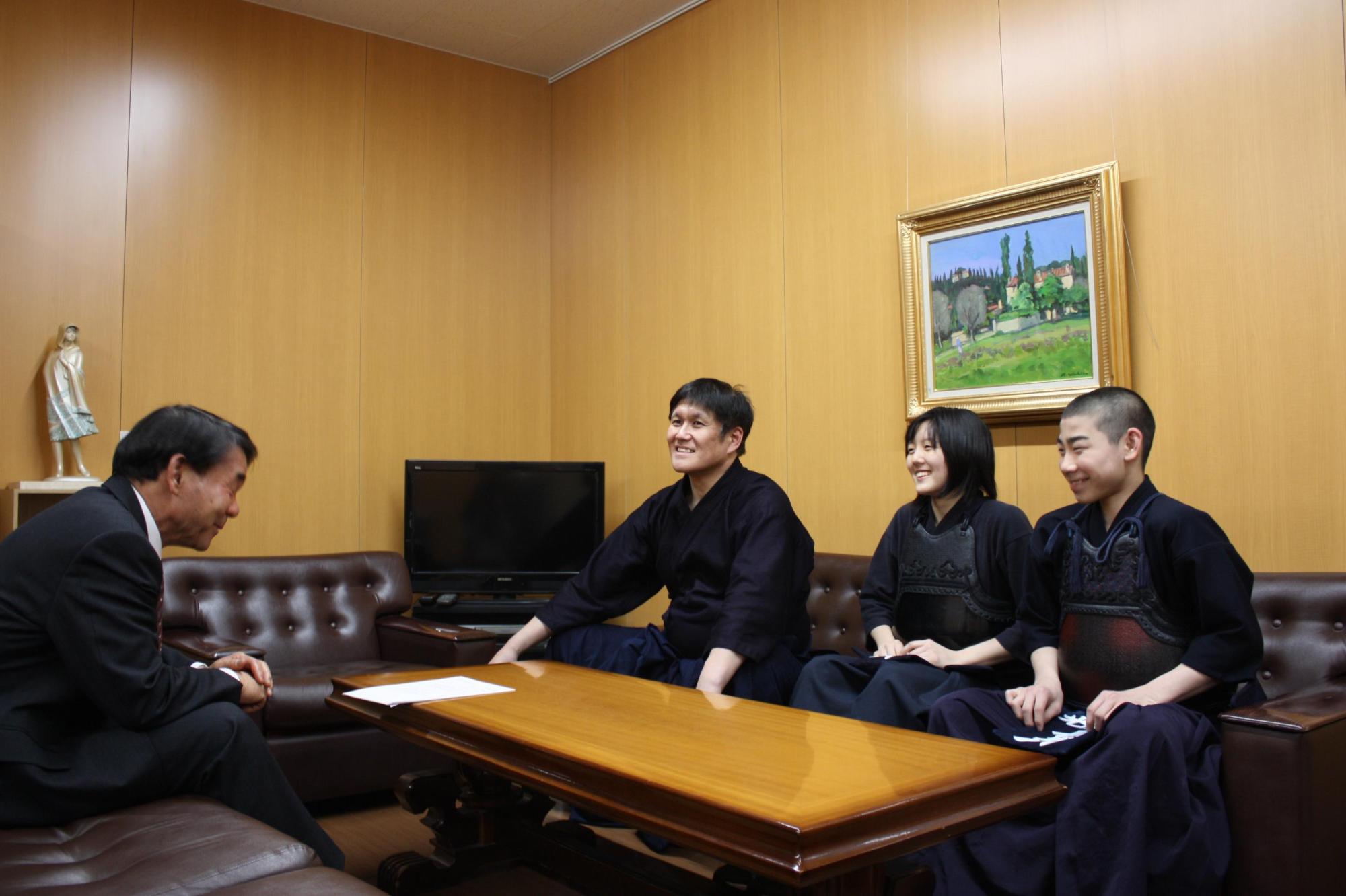 教育長と剣道着を着た二人の中学生と剣道着を着た大人が、机を挟んで話をしている写真。