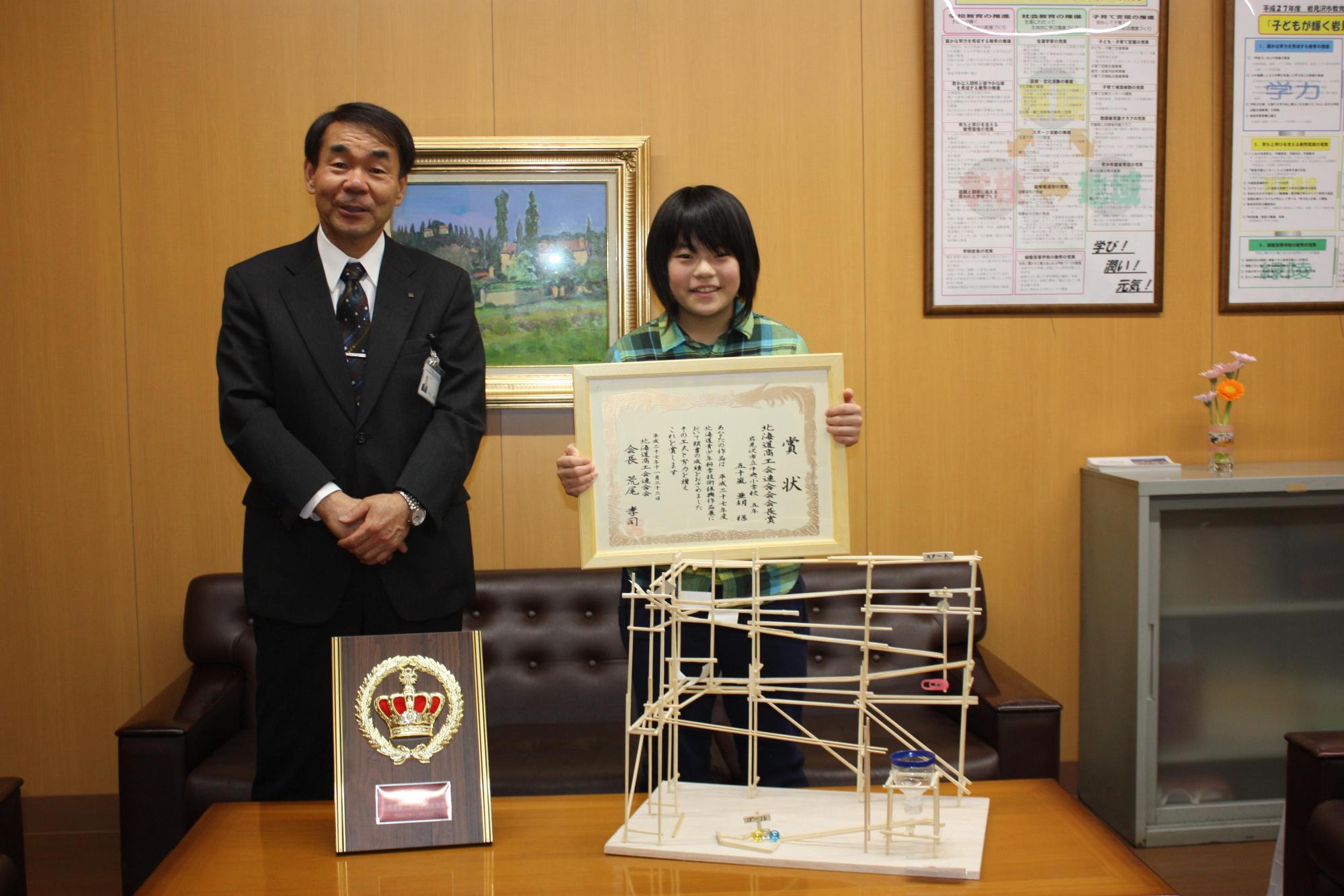 教育長と、賞状を持った小学生の子供と、わりばしビー玉コースターを撮影した写真。