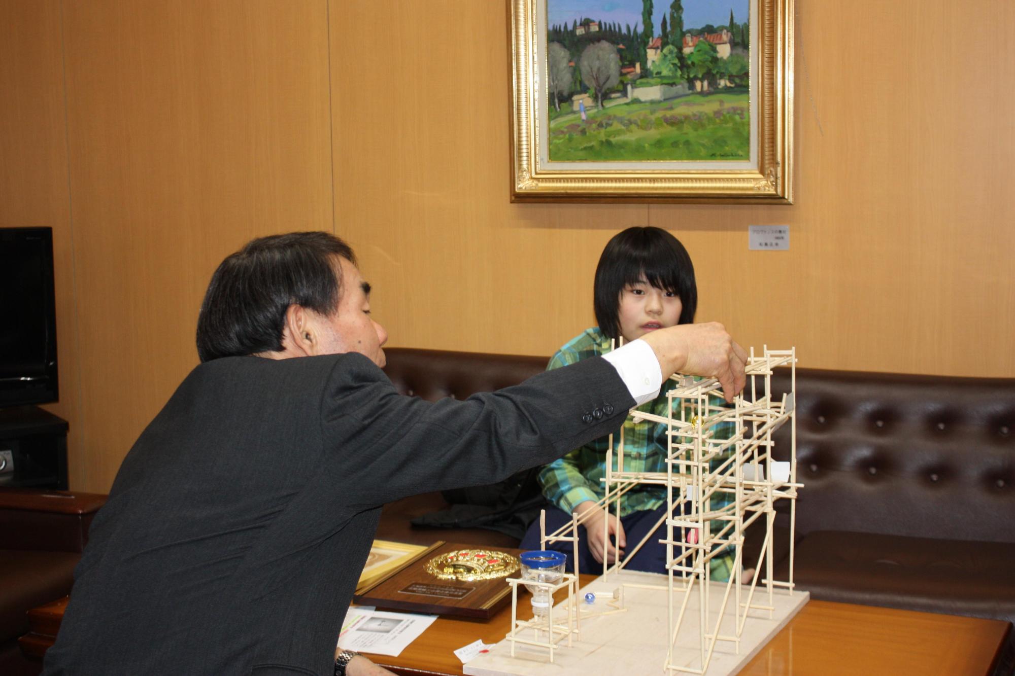 教育長が子供の前でわりばしビー玉コースターを見学している様子の写真。