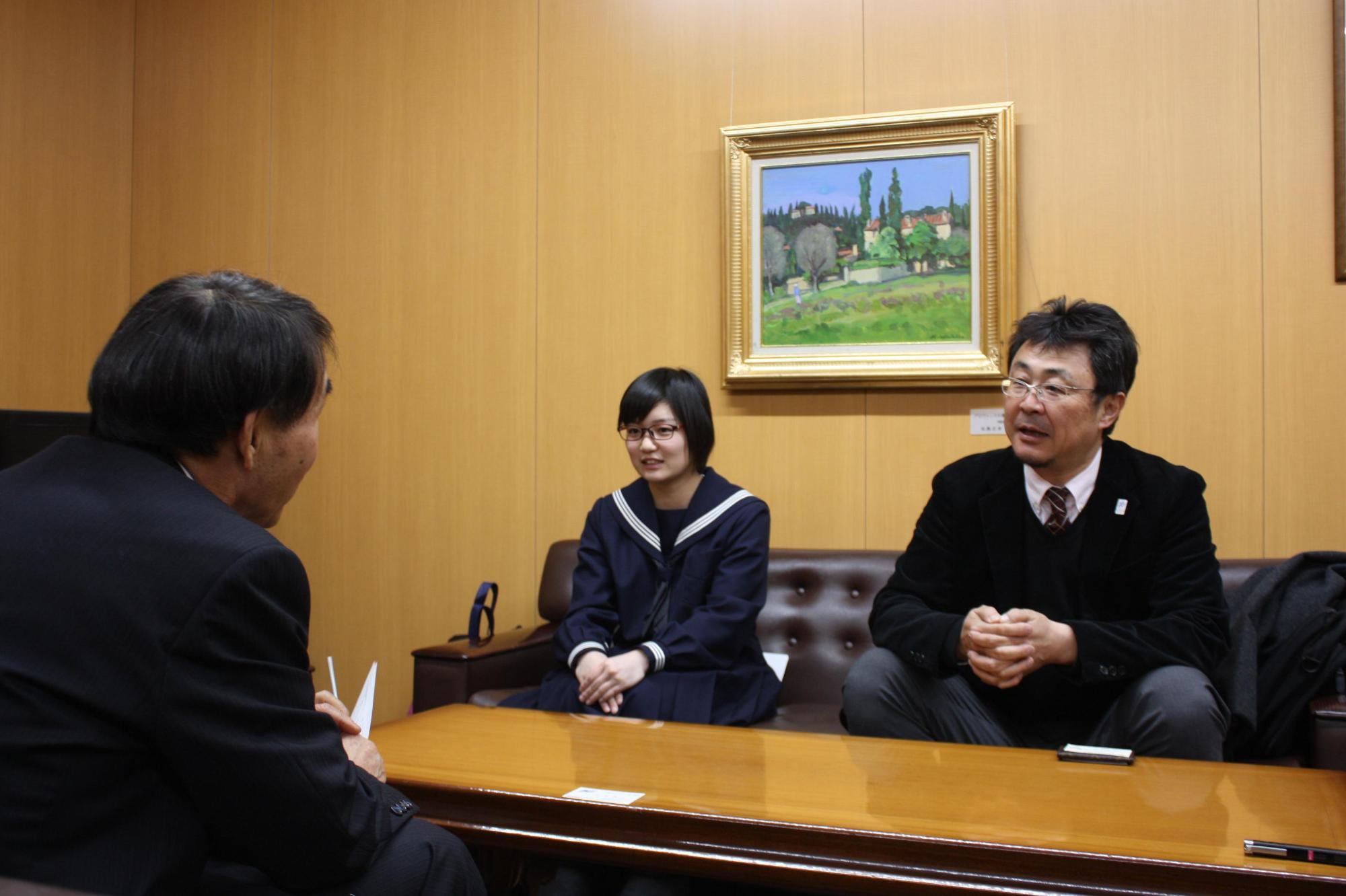 教育長と、セーラー服を着た中学生の女の子とスーツを着た男性の大人が机を挟んで話をしている写真。