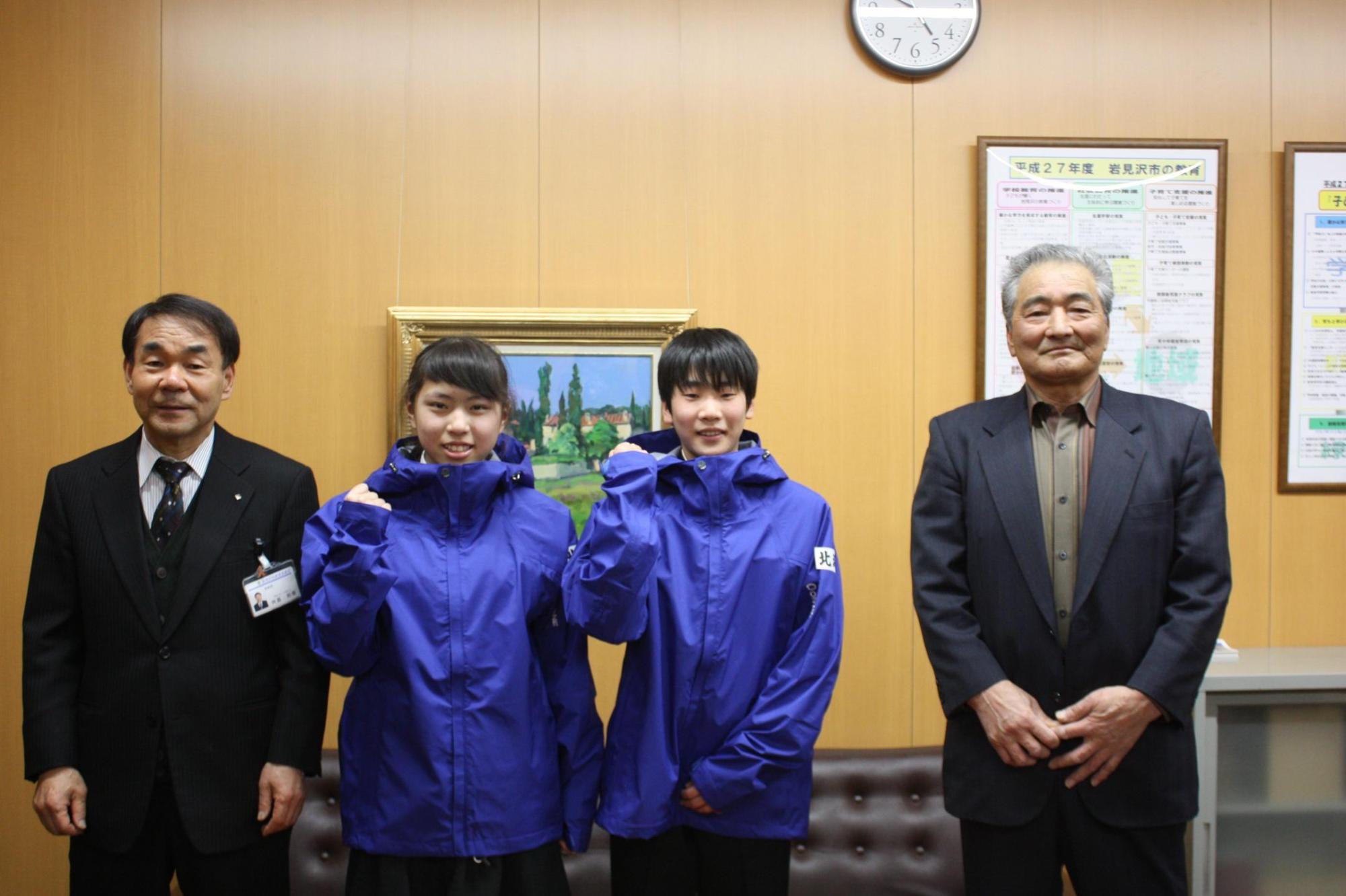 教育長、ウィンドブレーカー服を着た女の子と男の子、ジャケットを羽織った大人の男性が正面を向いて記念撮影をした写真。