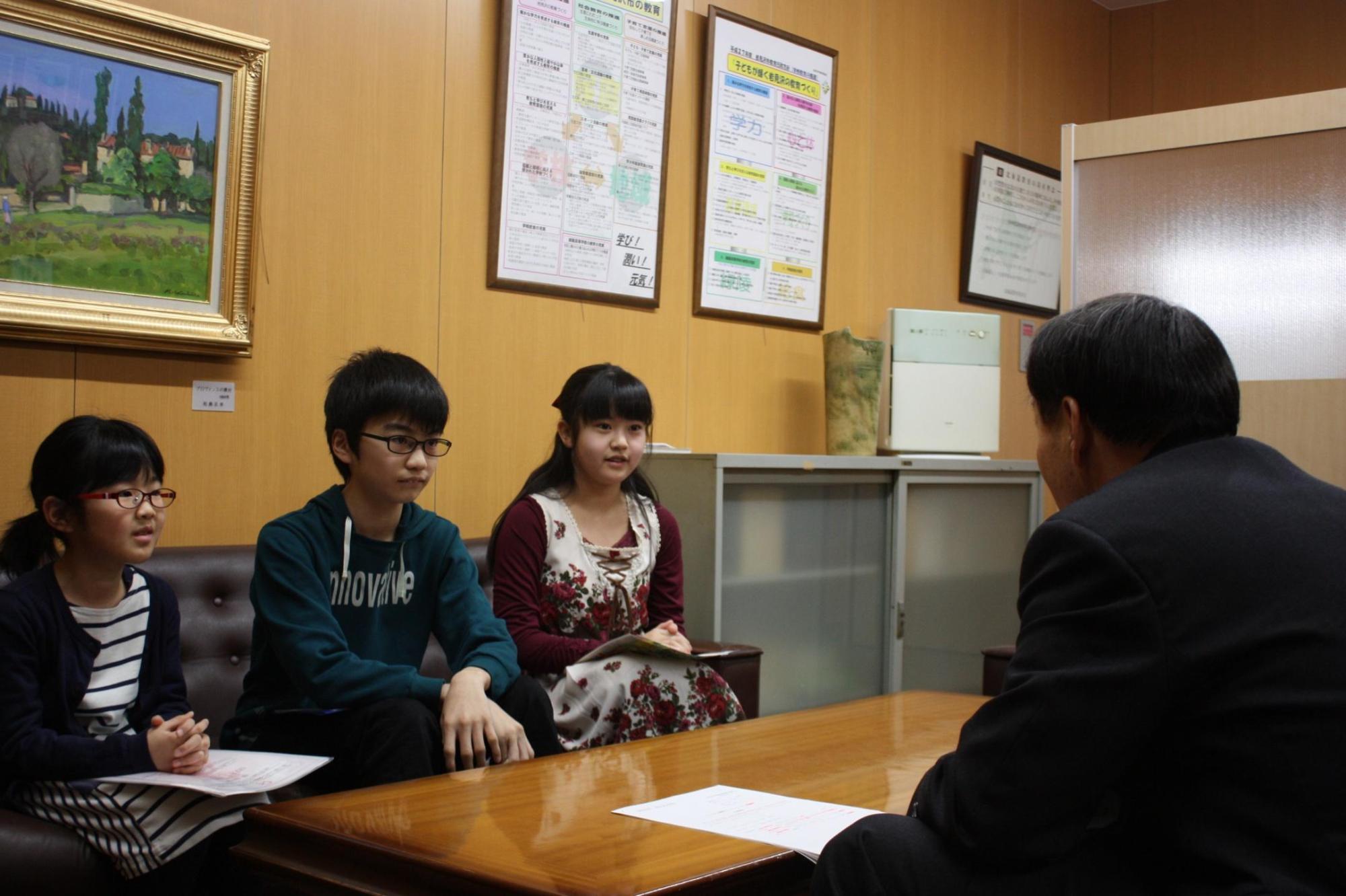 教育長と、3人の男女の子供達が机を挟んで話をしている写真。