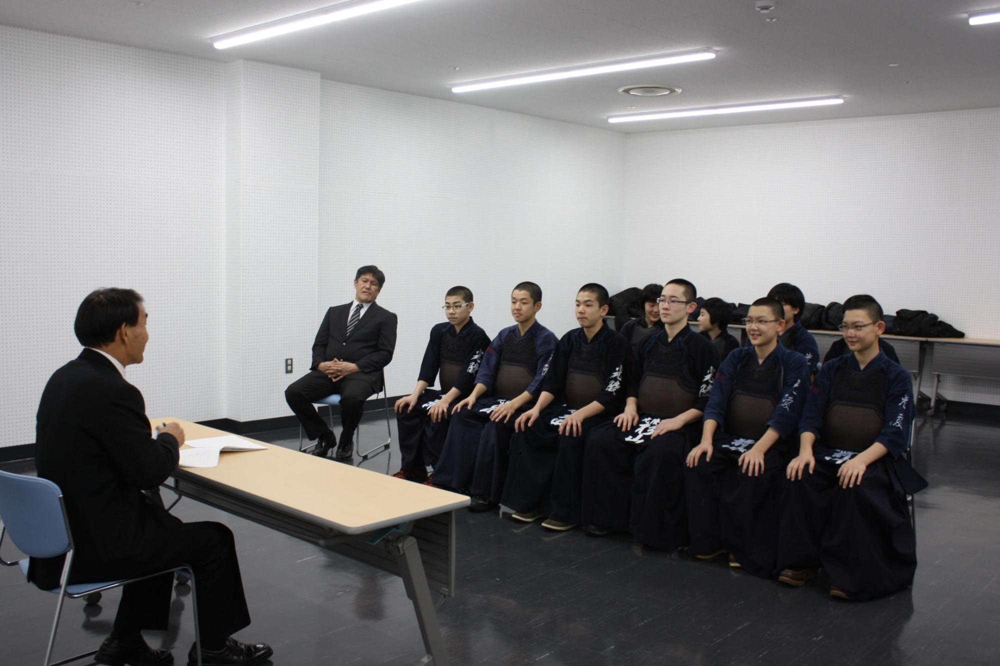 剣道着を着た中学生数人が、机を挟んで教育長の話を聞いている写真。