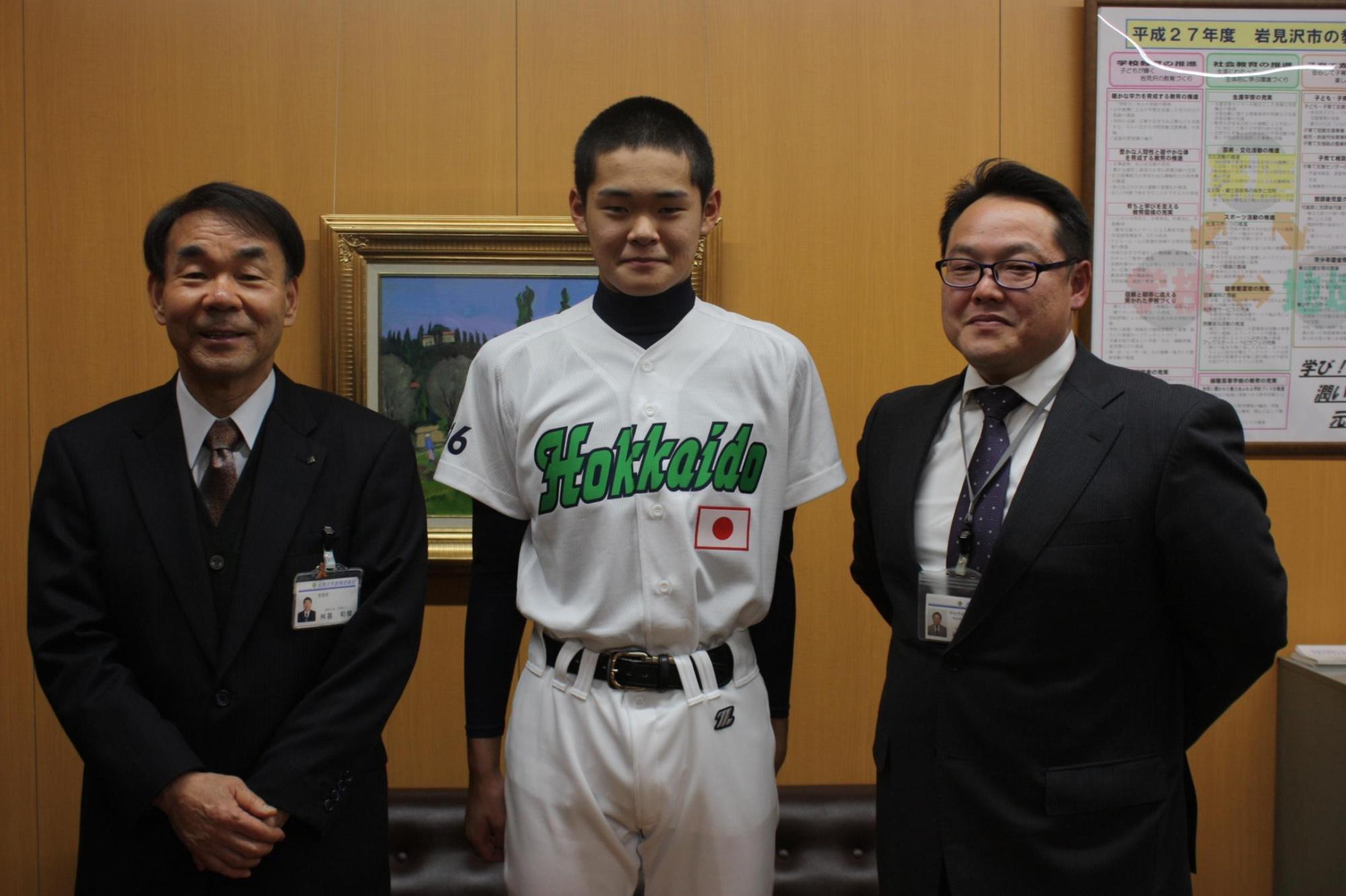 野球のユニフォームを着た子供、教育長、スーツを着た大人の3人で記念撮影をした写真。
