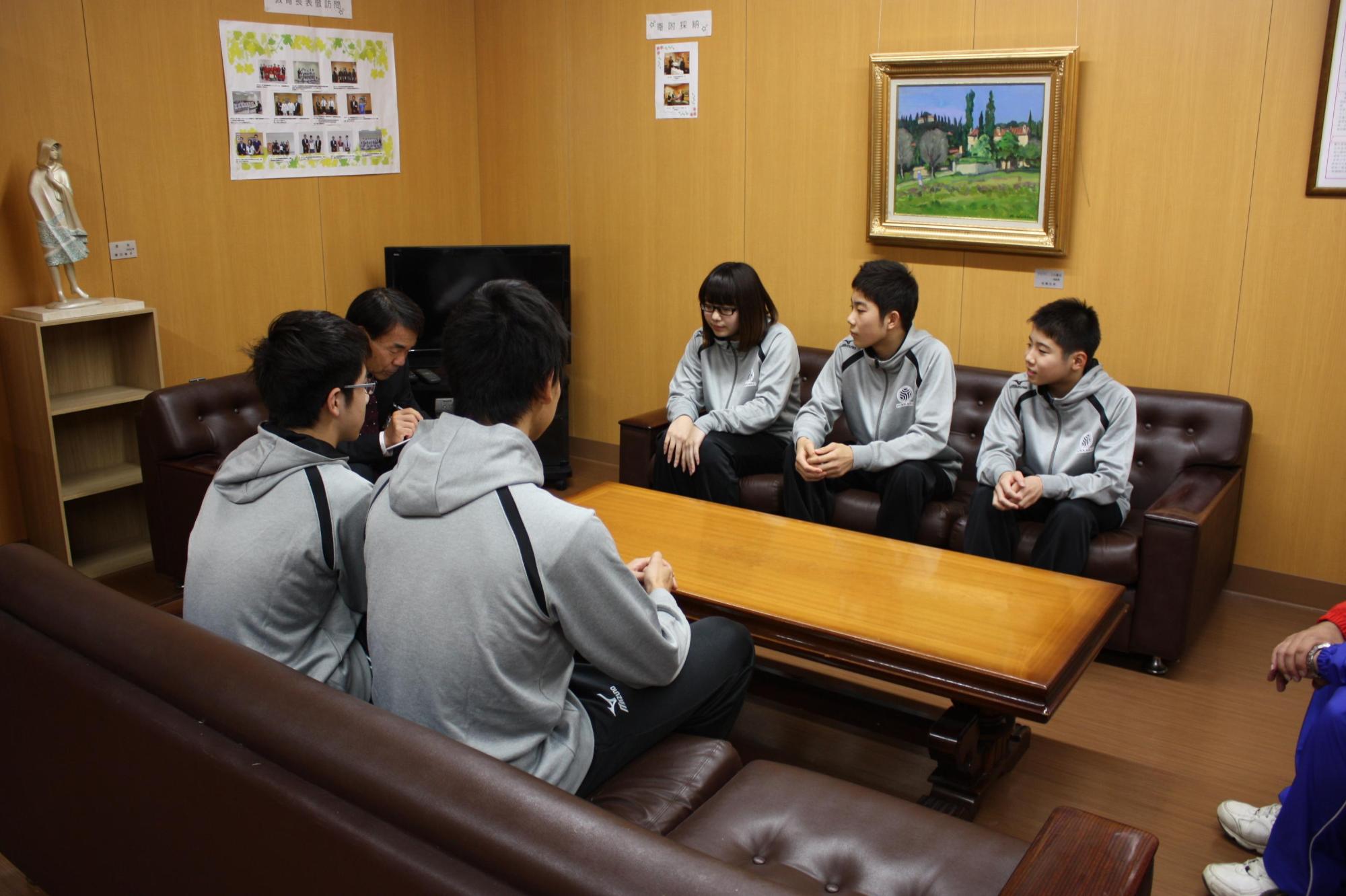 岩見沢市教育長を訪問し、ソファに座りながら話を聞いている井川 太陽さん、山下 俊哉さん、猪股 夕楓さん、石井 大智さん、笹谷 旺岐さんが映っている写真