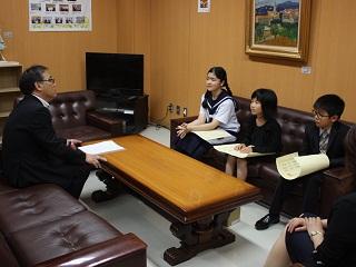岩見沢市教育長を訪問し、ソファに座りながら話を聞いている田村 結羽さん、地崎 孝平さん、佐藤 那留采さんが映っている写真