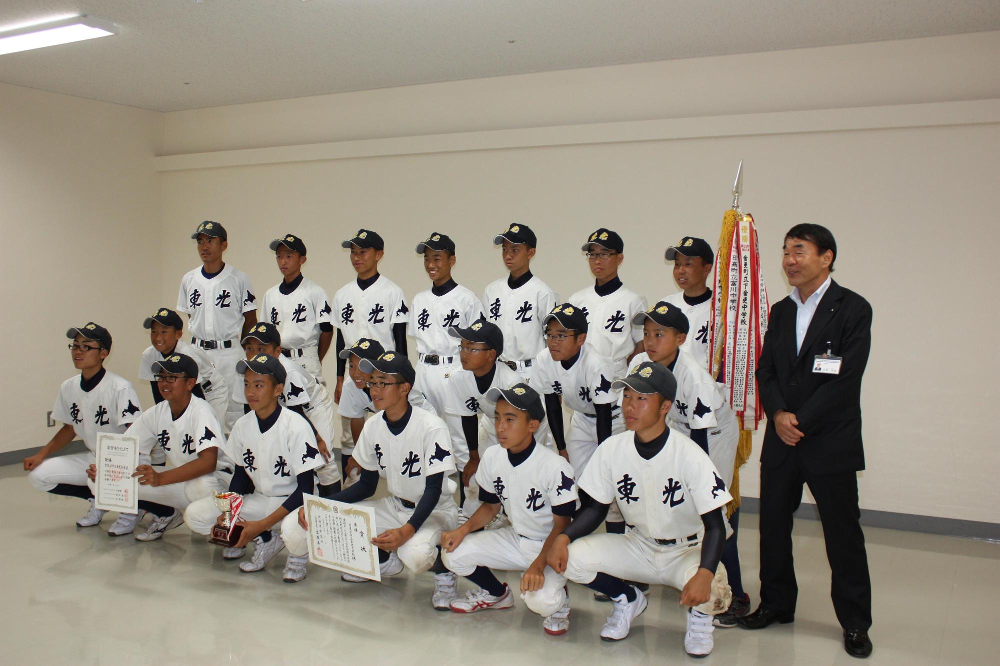野球のユニフォームを着た子供数人と教育長が記念撮影をした写真。