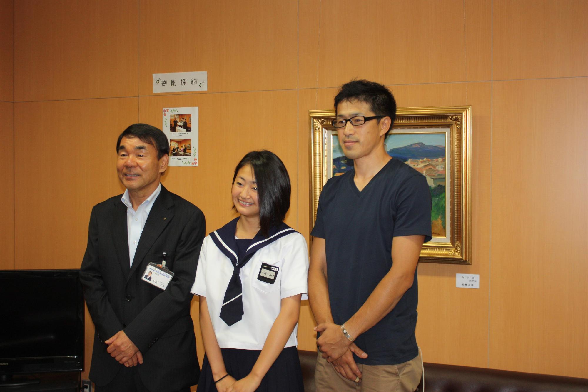 制服を着た谷川さん、男の人と教育長が記念撮影をした写真。
